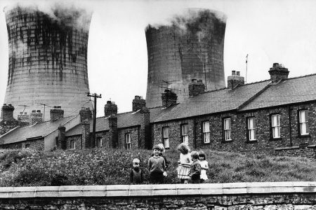Children posing for the photographer against the backdrop of workers' housing and industrial cooling towers, Teeside