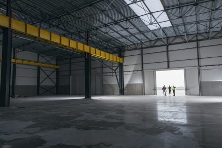 Architect team At Work Site With Blueprints standing at big hangar doors